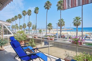 En balkon med blå stole, udsigt til stranden med palmer, og en klar blå himmel.