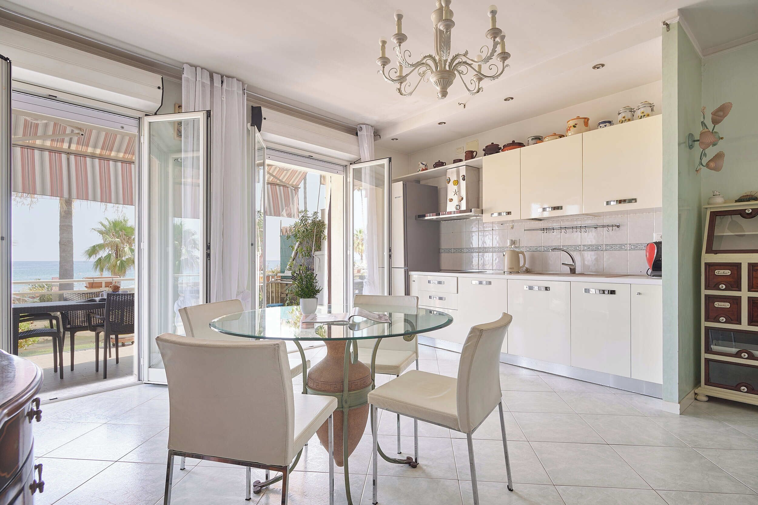 A modern kitchen with white cabinets, a glass dining table, and a view to the outside.
