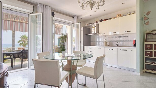 Una cocina moderna con armarios blancos, una mesa de comedor de vidrio y vistas al exterior.