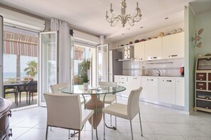A modern kitchen with white cabinets, a glass dining table, and a view to the outside. - Lo Scirocco (Andora)