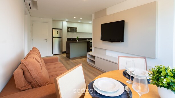 A modern living room with a sofa, a dining table set with plates and glasses, and a TV mounted on the wall. - Apart 2 Bedrooms at Praia Brava in Itajai Rvc0702 (Itajai)
