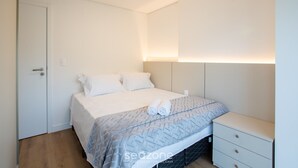 A neatly arranged bedroom with a bed, bedside table, and a door. - Apart 2 Bedrooms at Praia Brava in Itajai Rvc0702 (Itajai)