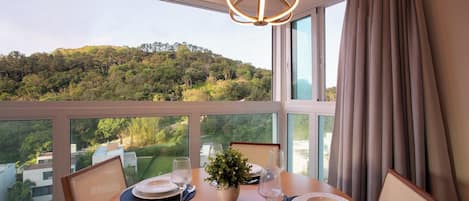 A dining area with a table set for two, a chandelier, and a view of a forested hill.