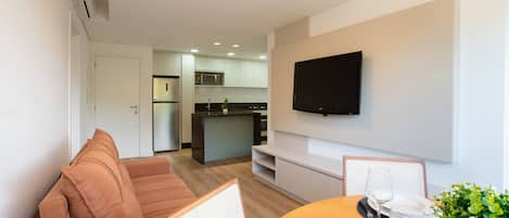 Una sala de estar moderna con un sofá, una mesa de comedor dispuesta con platos y vasos, y un televisor montado en la pared.