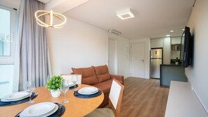 A modern, well-lit dining area with a round table set for two, a brown sofa, and a kitchen in the background. - Apart 2 Bedrooms at Praia Brava in Itajai Rvc0702 (Itajai)