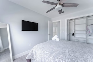 Ein Schlafzimmer mit Bett, Deckenventilator, Flachbildfernseher und begehbarem Kleiderschrank.