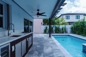 Eine moderne Außenküche mit Pool, Deckenventilator und Blick auf die Umgebung.