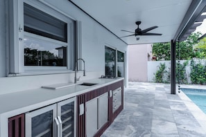 Eine moderne Außenküche mit integriertem Spülbecken, Deckenventilator und Blick auf einen Pool.