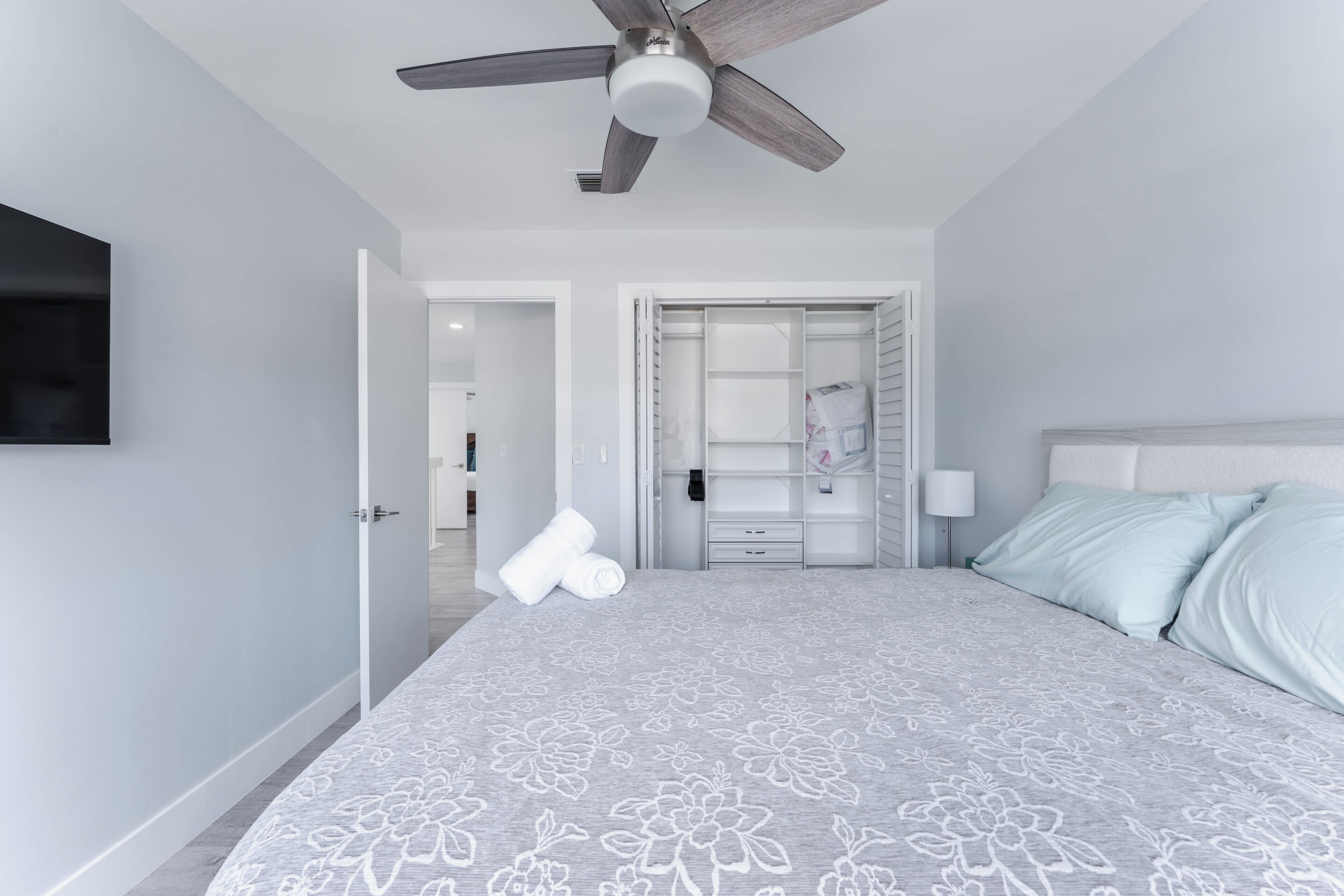 Une chambre à coucher comprenant un lit, un ventilateur de plafond, un téléviseur fixé au mur et un dressing.