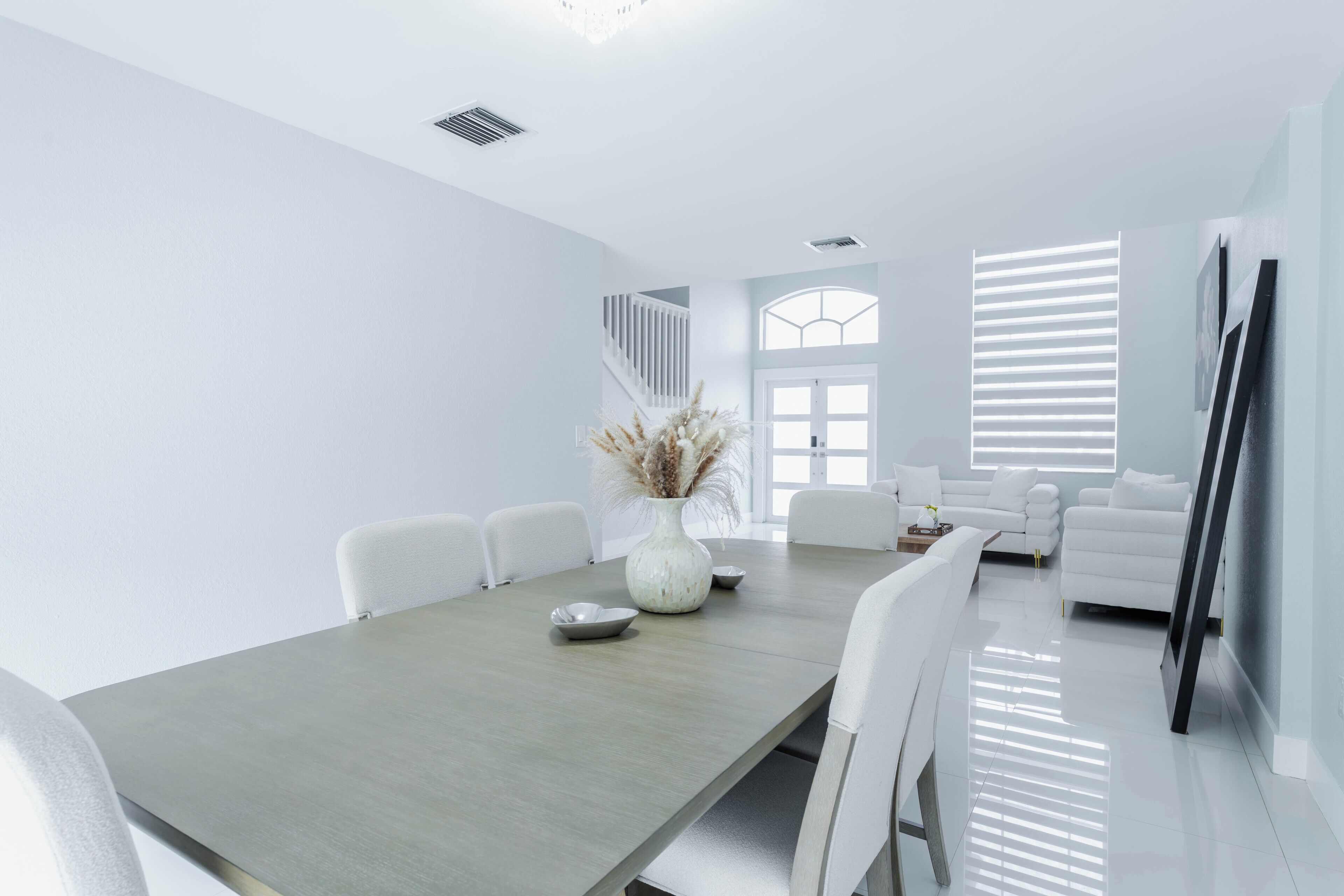 A modern, minimalist living space with a dining area, white furniture, and a staircase leading to an upper level.