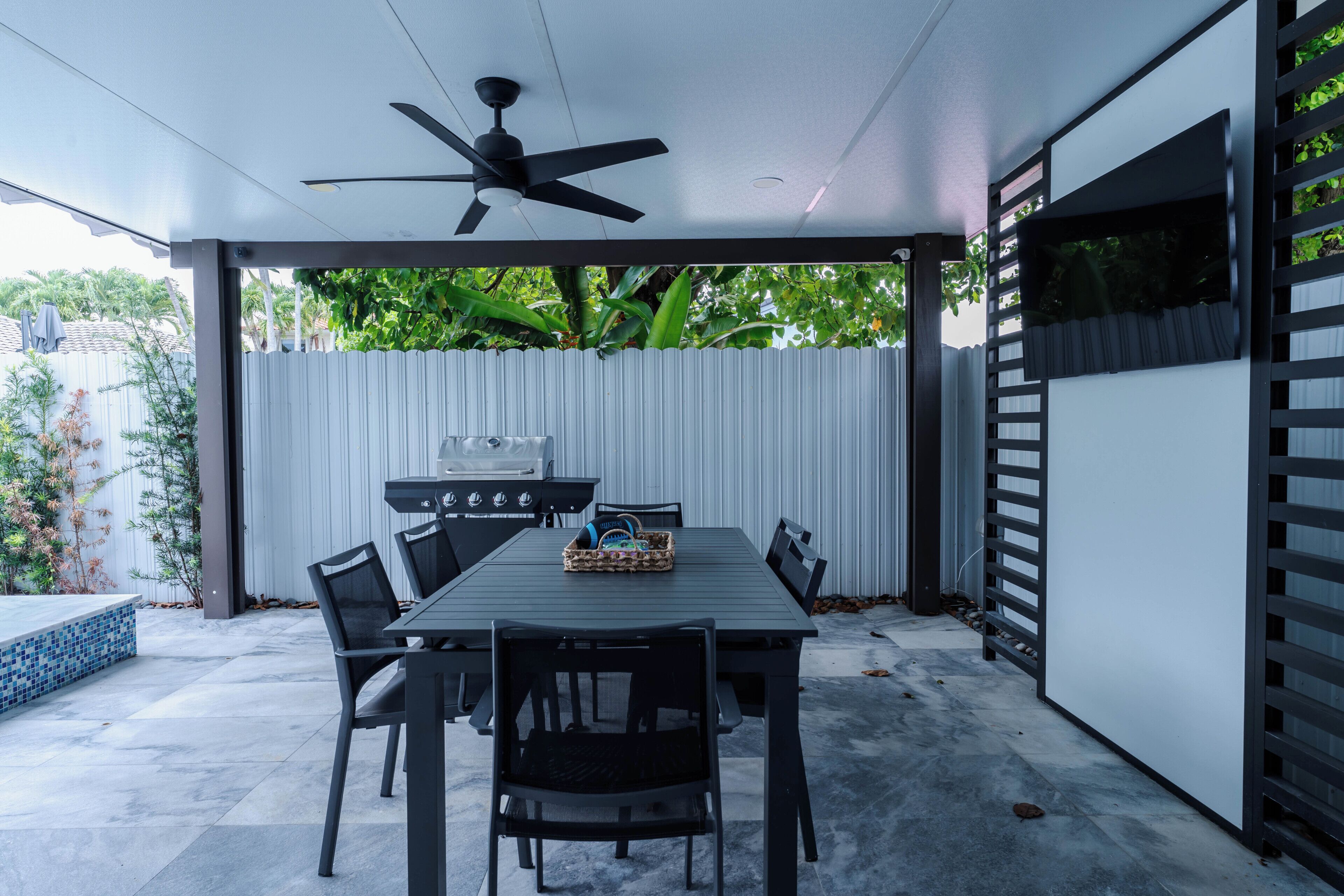 An outdoor patio with a table and chairs, a ceiling fan, and a grill.