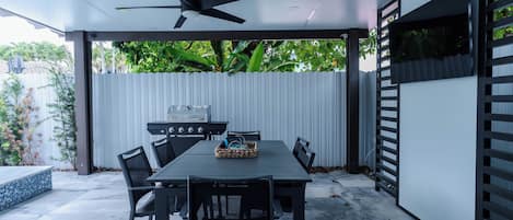 An outdoor patio with a table and chairs, a ceiling fan, and a grill.