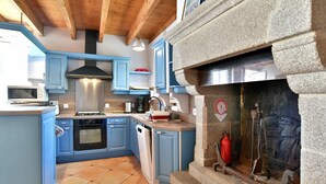 Una cocina con armarios azules, una estufa, un microondas y una chimenea de piedra con un extintor.