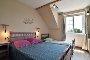 A bedroom with a sloped ceiling, a bed with a headboard, bedside tables, a hanging light fixture, and a window with curtains.
