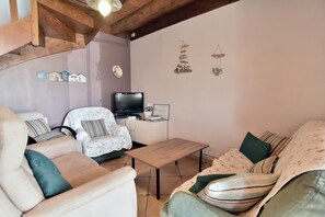 A cozy living room with a sofa, armchair, and a television. - Gîte L'Hydrangea - Jolie maison en pierre pour 6 (Saint-Pierre-de-Plesguen)