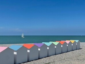 Una playa con una fila de sombrillas de colores y un velero a lo lejos.