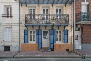 Un edificio de dos pisos con balcón, contraventanas y una puerta.