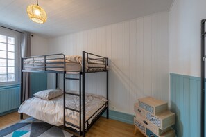 Une chambre avec un lit superposé, une fenêtre, une commode en bois et un luminaire suspendu.