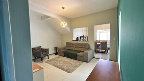 A living room with a sofa, armchair, and coffee table, a dining area with chairs and a table, and a kitchen area with appliances. - Spacious house - 650 meters from Atalaia Beach (Aracaju)