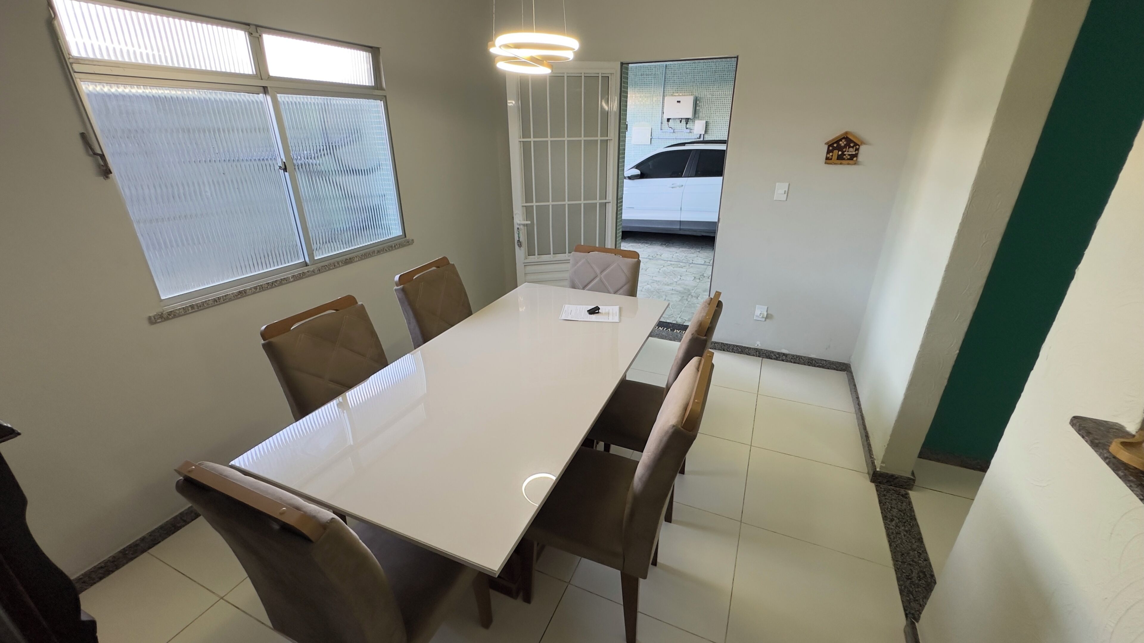 Un comedor con una mesa larga y seis sillas, una ventana con persianas y una lámpara de techo.