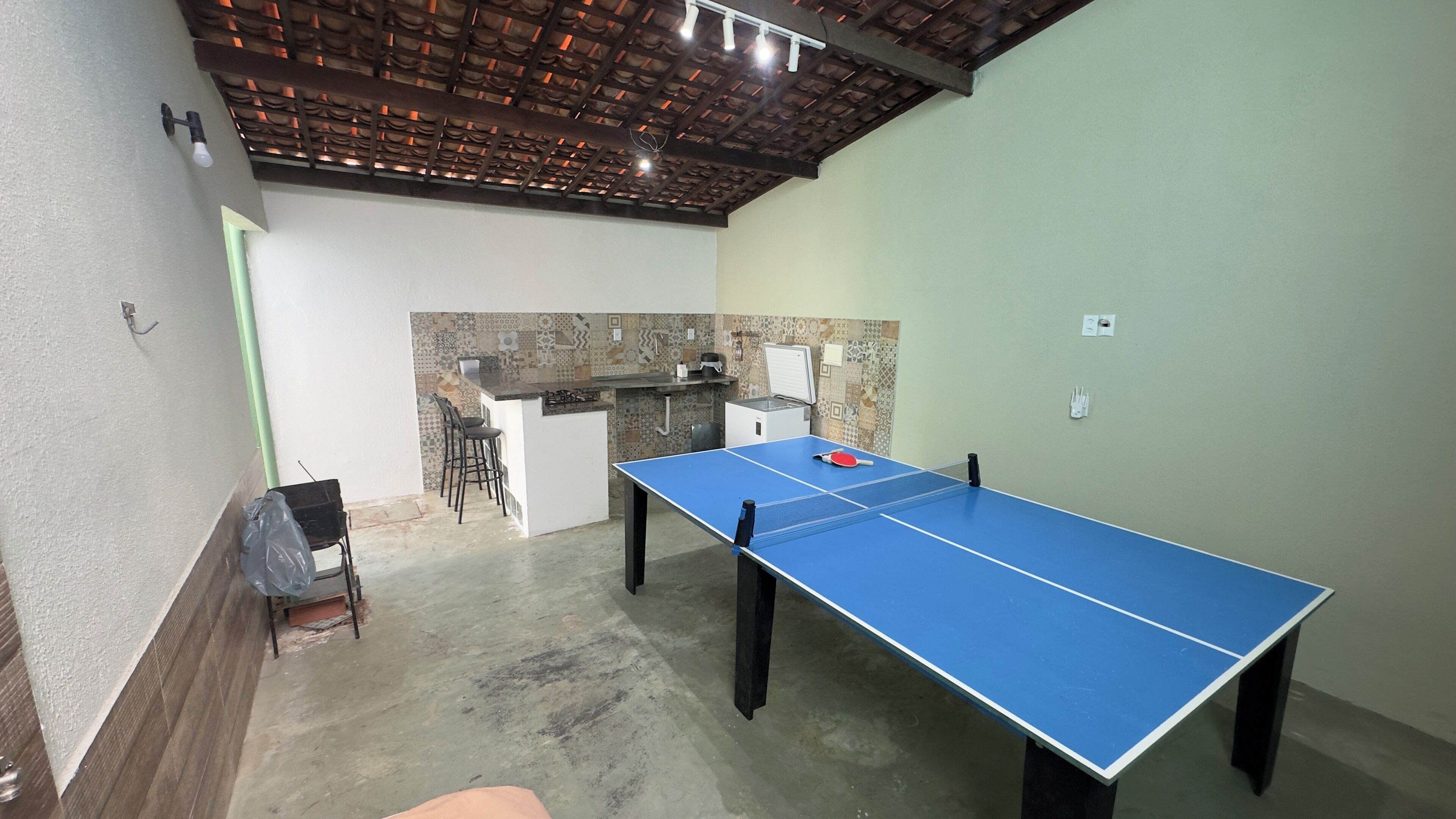 A room with a ping pong table, a small kitchen area, and a seating area with chairs.