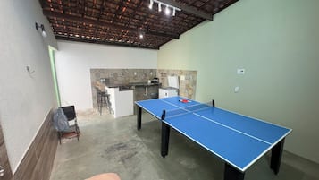A room with a ping pong table, a small kitchen area, and a seating area with chairs.