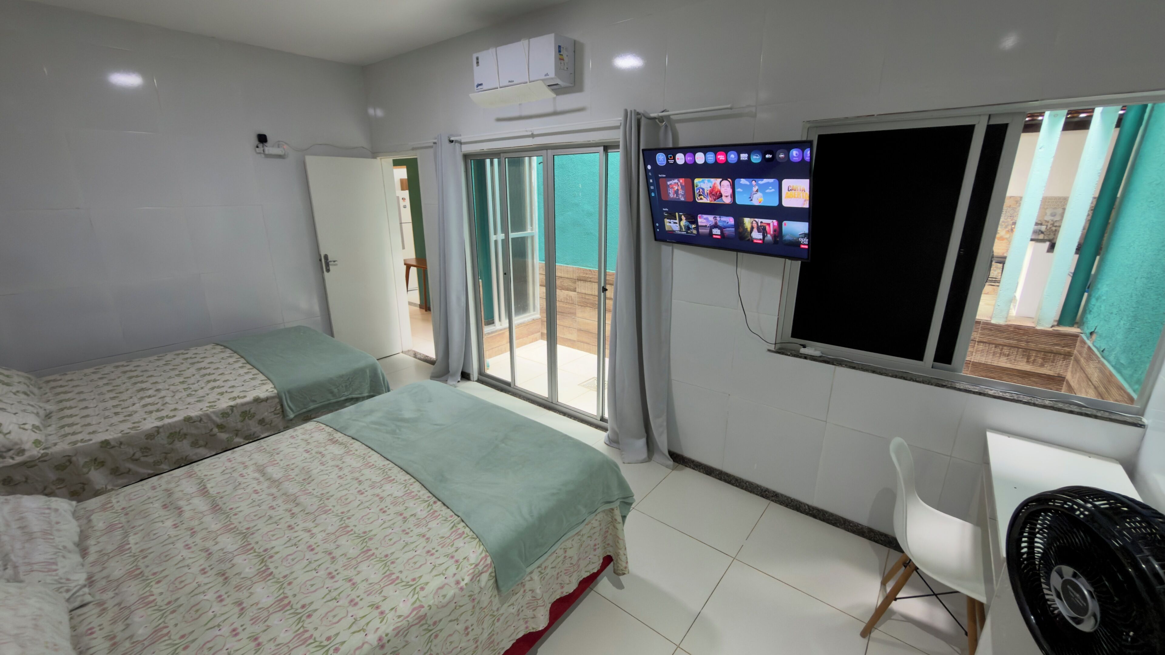 Een hotelkamer met twee bedden, een aan de muur bevestigde televisie en een schuifdeur naar een buitenruimte.