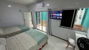 Habitación de hotel con dos camas, un televisor montado en la pared y una puerta corrediza de vidrio que da a un espacio exterior.
