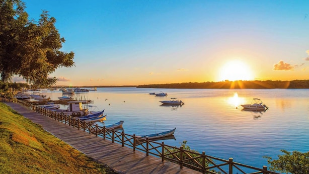 Un muelle de madera con barcos amarrados, un lago tranquilo y una puesta de sol al fondo.