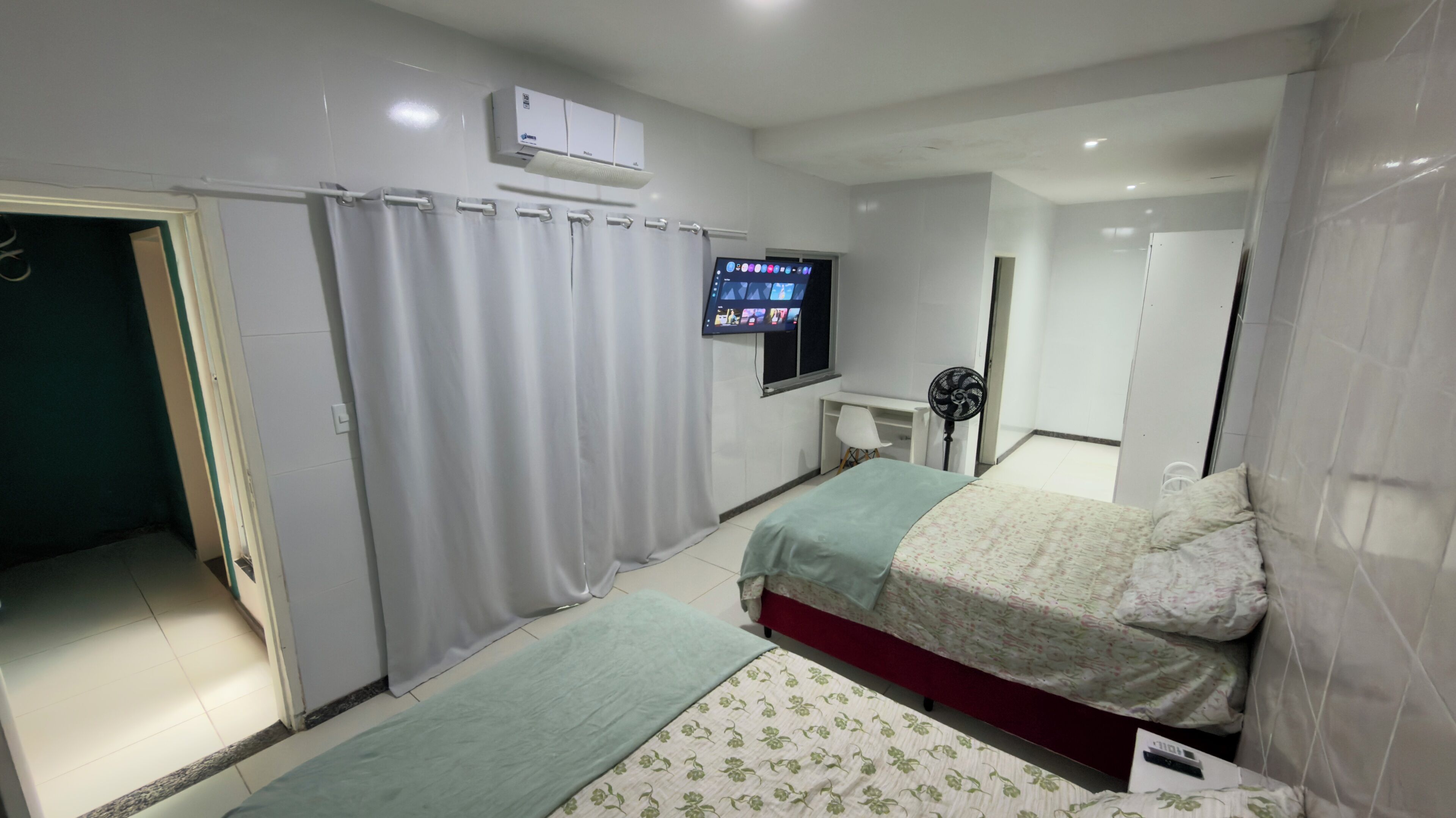 Een slaapkamer met een bed, een aan de muur bevestigde televisie, een bureau en een spiegel.