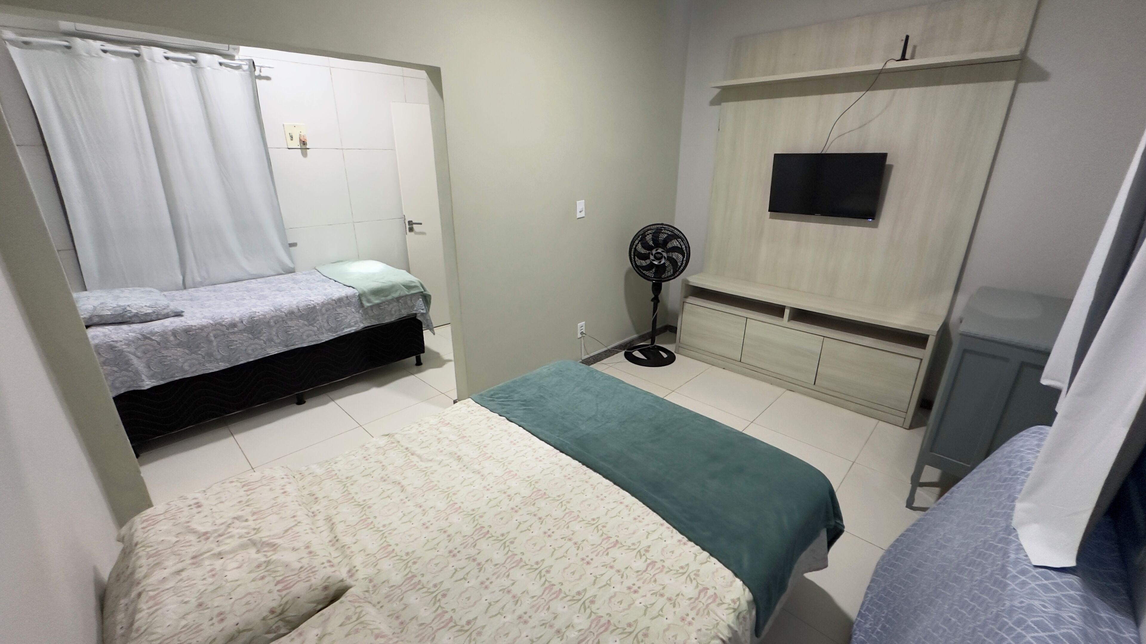 A bedroom with two beds, a TV, a fan, and a wardrobe.