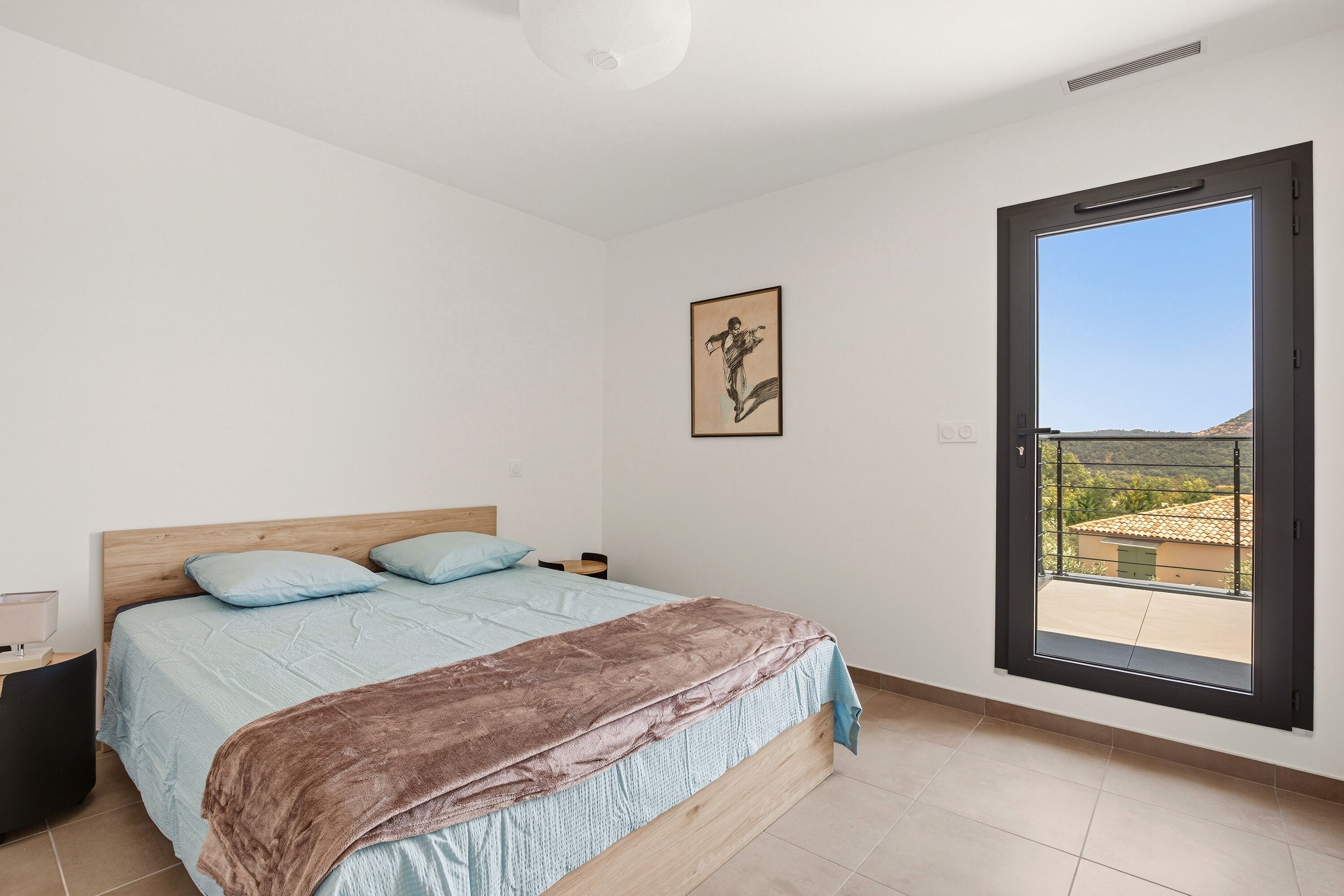 A bedroom with a bed, a nightstand, a table, a chair, a window with a view, and a ceiling light.
