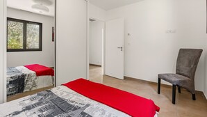 A bedroom with a bed, a chair, a wardrobe, and a door leading to another room. - Maison de la Seranne - Avec piscine (Le Bosc)