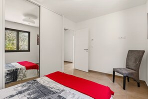 A bedroom with a bed, a chair, a wardrobe, and a door leading to another room. - Maison de la Seranne - Avec piscine (Le Bosc)