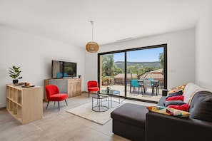 Un salon moderne comprenant un canapé, un fauteuil rouge, un téléviseur et un coin repas avec une table et des chaises.