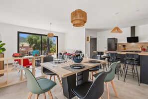 A modern kitchen with a dining area, large windows, and a view of the outdoors. - Maison de la Seranne - Avec piscine (Le Bosc)