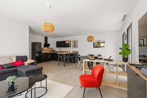 A modern living space with a sofa, dining table, kitchen area, and a red chair. - Maison de la Seranne - Avec piscine (Le Bosc)