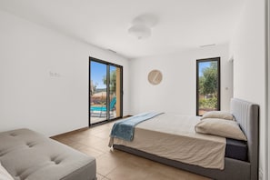 A modern bedroom with a bed, a sofa, and a view of the outdoors through large windows. - Maison de la Seranne - Avec piscine (Le Bosc)