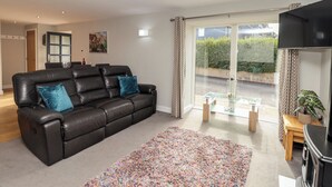 Een woonkamer met een zwarte leren bank, een kleurrijk vloerkleed, een glazen tafel en een schuifpui naar een tuin.