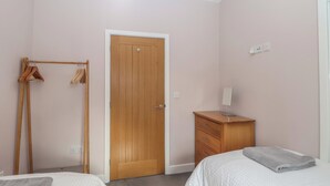 Een slaapkamer met twee bedden, een houten garderobe, een garderobe met kleren, en een houten deur.
