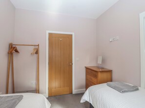 A bedroom with two beds, a wooden wardrobe, a wooden wardrobe with clothes, and a wooden door. - The Old Dairy (Liskeard)