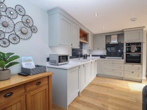 A modern kitchen with white cabinetry, a built-in microwave, and a coffee machine. - The Old Dairy (Liskeard)