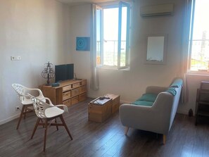 A living room with a sofa, a television, a wooden cabinet, and a window. - Appartement climatisé avec vue mer et sur les toits du vieux Grasse (Grasse)