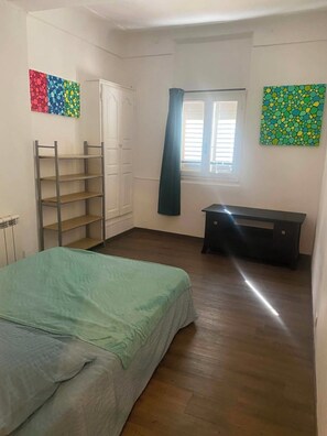 Une chambre à coucher comprenant un lit, une armoire, un banc et deux fenêtres avec des rideaux.