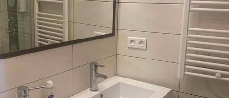 A bathroom with a double sink, a mirror, a towel rack, and a toilet.
