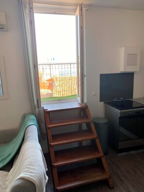 Ein Zimmer mit einer Holzleiter, die zu einem Balkon führt, einem Fernseher auf einem Tisch und einer Mülltonne.
