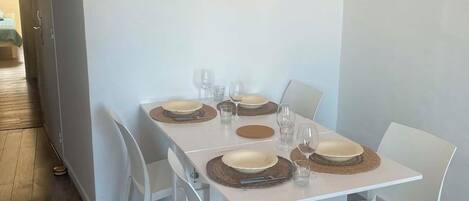 A dining area with a rectangular table set for four, white chairs, and a wooden floor.
