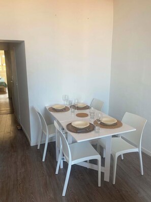 Ein Essbereich mit einem rechteckigen Tisch, gedeckt für vier Personen, weißen Stühlen und Holzboden.