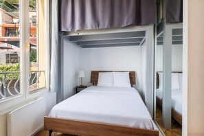 A bedroom with a bed, a nightstand, a lamp, a window, and a view of the outside. - Le balcon d'Anselmetti - Proche Plage (Cap-d'Ail)
