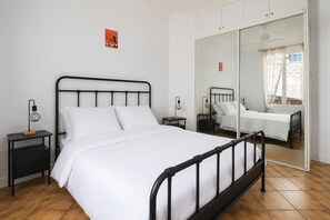 Une chambre à coucher avec un lit, deux tables de chevet, un miroir et une fenêtre avec des rideaux.